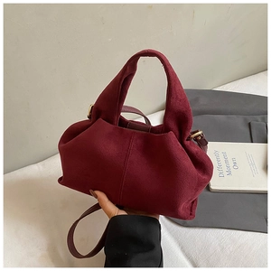Detail of burgundy suede bucket bag with fine shoulder strap and golden hardware