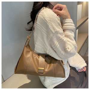 Detailed close-up of brown leather shoulder bag with metallic buckle on a white sweater