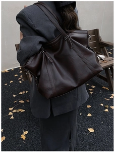 Detailed view of the large chocolate brown PU leather tote bag worn by a model in autumn