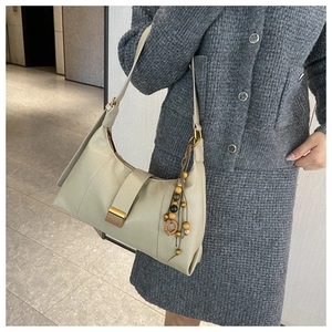 Detail of light beige shoulder bag featuring golden metal clasp and retro beaded charm