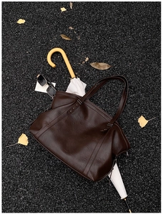 Dark brown leather tote bag on street floor with autumn leaves and stylish accessories