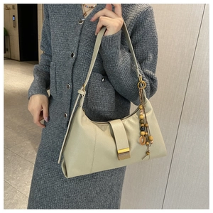 Detail of beige leather shoulder bag with gold metal buckle and wooden bead charm accessory