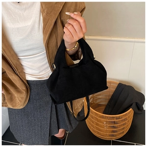 Detail of a black suede handbag featuring a pleated design and slim shoulder strap