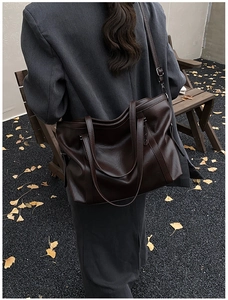 Detail of a dark brown glossy leather tote bag with fallen ginkgo leaves on a pebble path