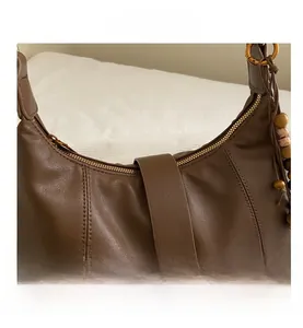 Detail of brown leather bag featuring vertical stitching and a wood bead tassel zipper