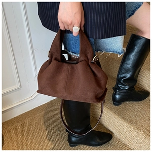 Detail of coffee brown suede bucket bag featuring elegant pleats and metal ring hardware