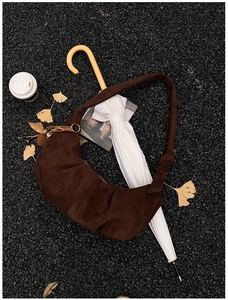 Detailed close-up of dark brown suede crescent bag with tassels on asphalt texture