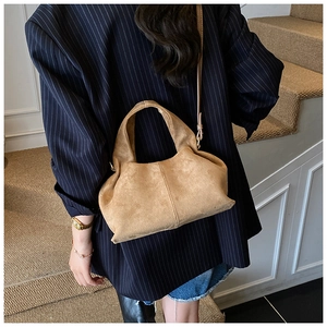 Detail of a brown suede bucket bag with soft pleats and a unique top handle design