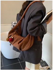 Detail of brown suede hobo bag with a plush pompom charm in a cozy indoor setting