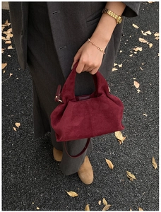 Detail view of burgundy suede cloud bag with top handle and strap on autumn leaf ground