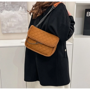Detail of brown quilted shoulder bag with faux fur trim and metal chain strap worn by a model
