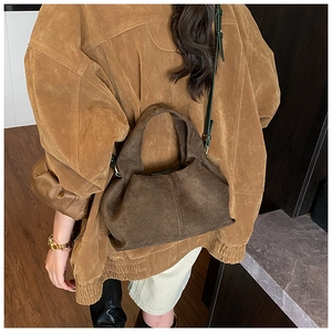 Detail of dark brown suede crescent handbag with slim crossbody strap on model