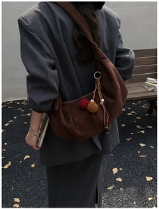 Detail of a brown faux suede crescent bag with plush pom-poms and tassel accents