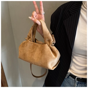 Detail of caramel suede handbag with gold hardware and shoulder strap on model