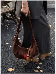 Detail of suede half-moon bag in brown with decorative fuzzy ball charm