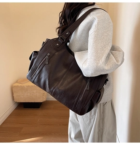 Detail of dark brown leather tote bag showing grainy texture and vertical zipper pockets