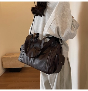 Detail of dark brown tote bag with side flap pocket and multiple zippers on leather surface