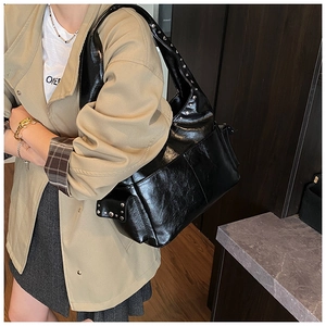 Detail view of silver rivets and functional side pocket on black shiny shoulder bag