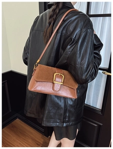 Close-up of retro brown patchwork shoulder bag with large brass buckle on leather coat