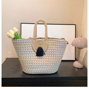 Detail of hand-woven straw tote bag with black tassels on a minimalist wooden counter