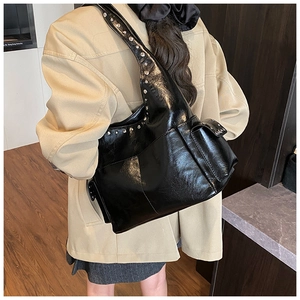 Rear view of a model wearing a black patent leather hobo bag with silver rivets and wide strap