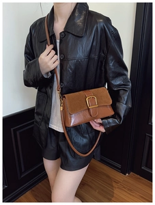 Detailed view of brown leather crossbody bag with vintage buckle on a leather jacket