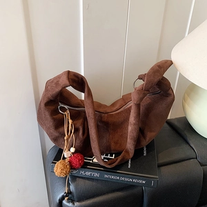 Detail of suede crescent bag showing knot handle texture and plush ball charm decoration