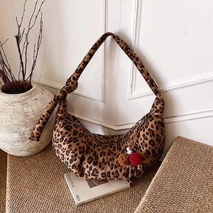 Detail of leopard print hobo bag with red pompom charm and knotted strap on a table