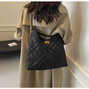 Rear view of a model wearing a black quilted leather hobo bag with a gold metal chain strap