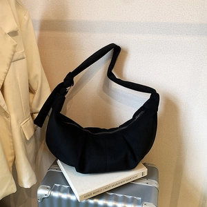 Detail of black pleated canvas crescent bag with wide knotted strap and metal zipper closure