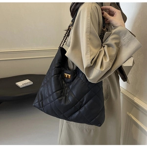 Detail of black quilted leather tote with golden twist-lock closure and chain strap