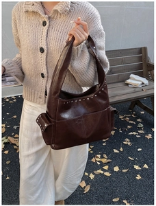 Detail of dark brown vintage rivet shoulder bag on a park bench during autumn