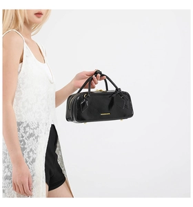 Close-up of black glossy leather baguette bag with golden logo and zipper details
