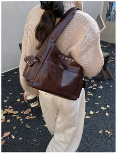 Detail of dark brown glossy leather shoulder bag with vintage rivets and side pocket
