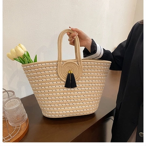 Detail of hand-woven straw tote bag with black tassels and decorative yellow tulips