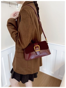 Detail of burgundy leather shoulder bag with vintage gold buckle on brown suit