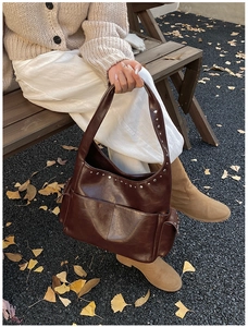 Close-up of vintage brown shoulder bag with silver rivets and front pockets in autumn park