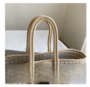 Detail of woven straw tote bag with reinforced handles and decorative black tassels
