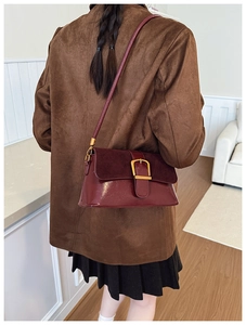 Detailed view of deep red crossbody bag featuring a golden horse-shoe buckle detail