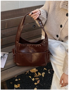 Detail of dark brown vintage hobo bag with silver rivets on a wooden bench outdoors