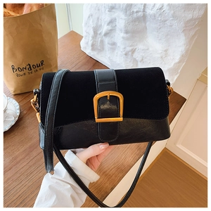 Detailed view of black flap bag with gold square buckle on a wooden tabletop
