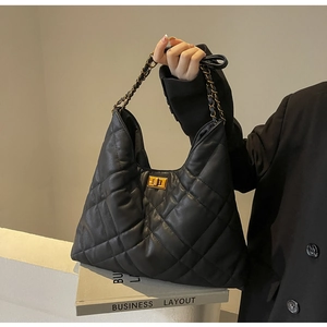 Detail of black quilted chain bag with gold rotary clasp and leather strap held by a model