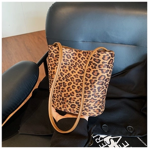 Detailed view of leopard print bucket bag with brown handles on a dark leather chair