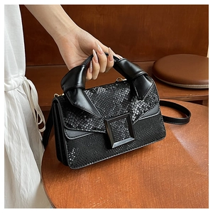 Detail of black faux snakeskin handbag featuring a knotted handle and square buckle deco