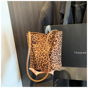 Detailed view of leopard print bucket bag with dual straps held against a dark suit