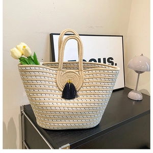 Detail of woven tote bag with cream stripes, black tassels, and rustic circular texture