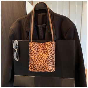 Detail of leopard print bucket bag with brown leather straps against a black coat