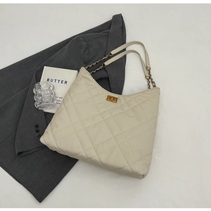 Detail of cream quilted tote bag featuring a gold square twist lock and metal chain strap
