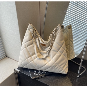 Detail view of white quilted tote bag featuring metallic chain strap and gold turn-lock