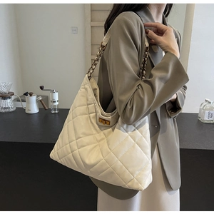 Macro view of beige quilted hobo bag featuring a gold chain strap and metal swivel lock